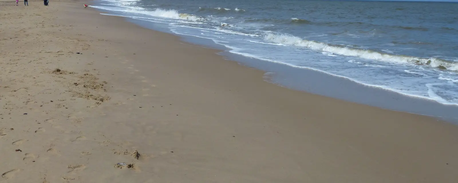 A long sandy beach with waves breaking on a clear day